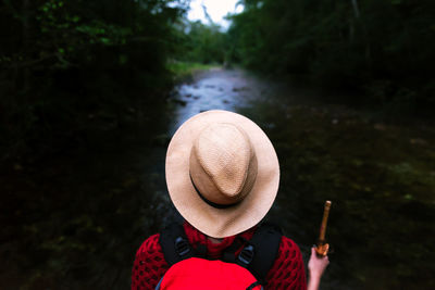 Back view of anonymous wanderer with backpack standing on trail in dark woods during summer adventure