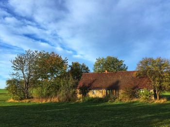 House on field by trees against sky