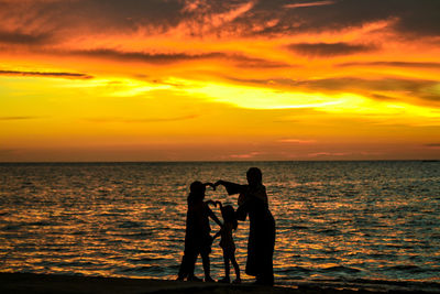 Silhouette men standing on beach against sky during sunset