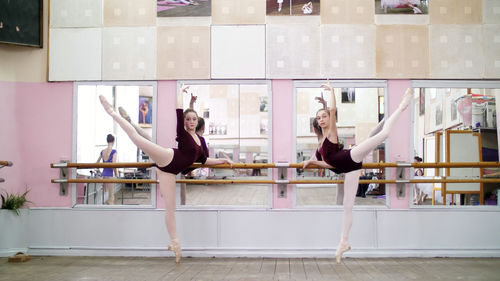 In dancing hall, young ballerinas in purple leotards perform grand battement back on pointe shoes