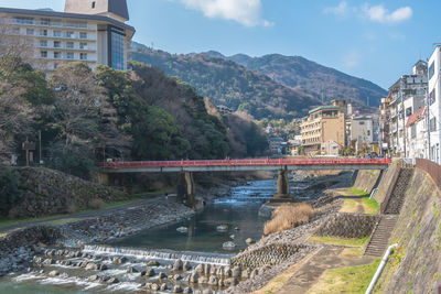 Bridge over river by buildings in city against sky