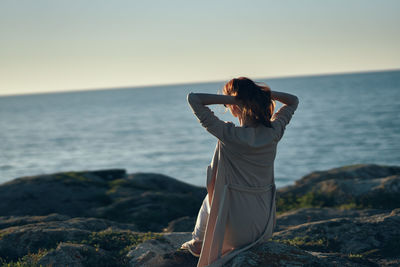 Woman standing in sea against sky during sunset