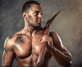 Shirtless muscular worker holding pick axe against wall