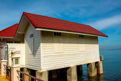 Red stilt house by sea against sky