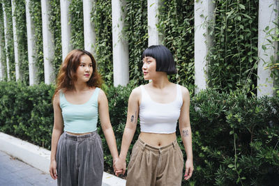 Beautiful young lesbian couple standing against plants outdoors