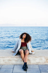 Young woman sitting in sea against sky