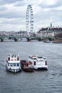 Boats in river by cityscape against sky