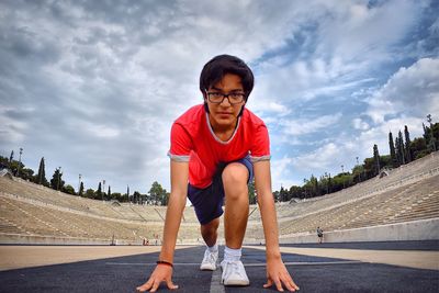 Full length portrait of teenage boy on running track against cloudy sky