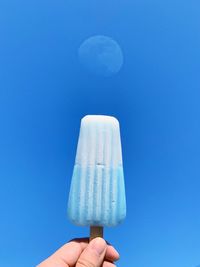 Close-up of hand holding ice cream against blue background