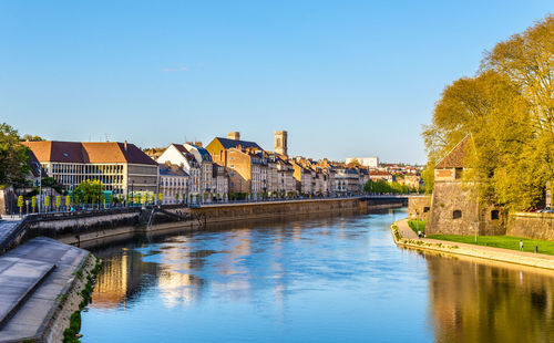 Bridge over river by buildings against blue sky