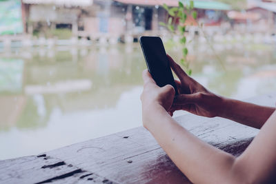 Cropped image of hands photographing lake through mobile phone