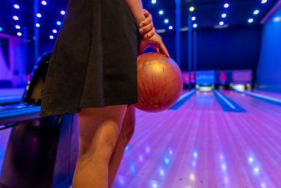 Midsection of woman holding ball while standing in illuminated room