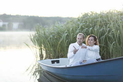 Romantic couple enjoys time sitting in boat, sailing in water,pointing fingers away. happy smiling