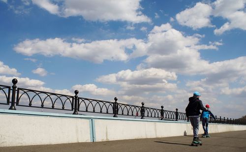 Rear view of boys skateboarding on bridge against sky