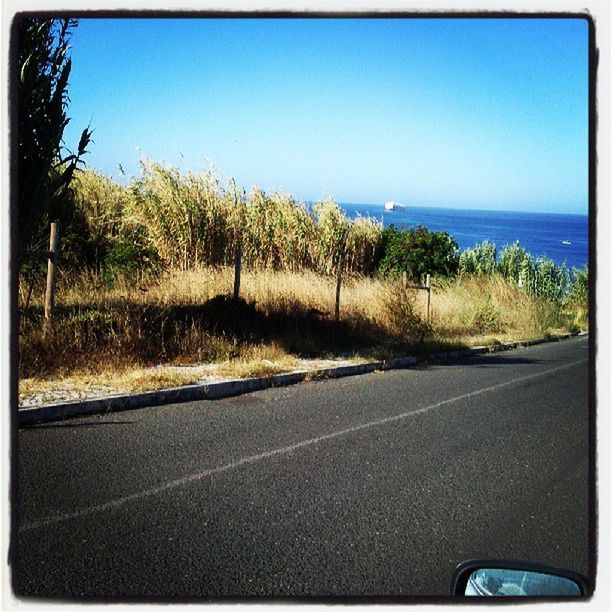 road, clear sky, transportation, blue, road marking, sea, transfer print, copy space, horizon over water, nature, street, asphalt, tranquil scene, water, sky, tranquility, beauty in nature, auto post production filter, tree, the way forward