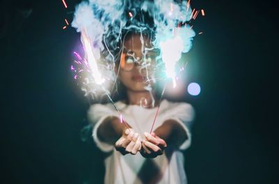 Woman holding lit sparklers at night