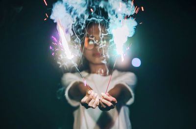 Portrait of woman holding illuminated lighting equipment at night