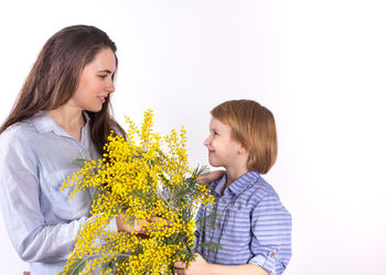 Young woman holding yellow flower against white wall