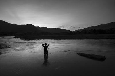 Rear view of silhouette person standing in lake against sky