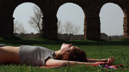 Young woman relaxing on grassy field against old ruin