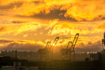 Silhouette cranes against orange sky