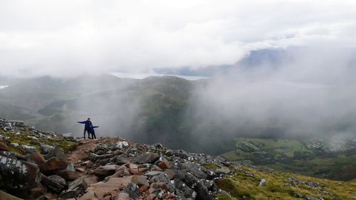 High angle view of father and son standing on cliff against mountains