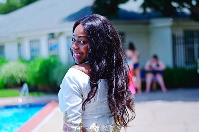 Rear view portrait of smiling young woman standing at poolside