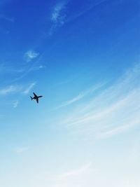 Low angle view of silhouette airplane against blue sky