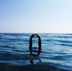 Hands forming heart shape at blue sea