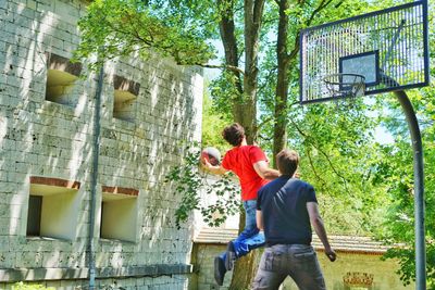 Rear view of men playing basketball against trees