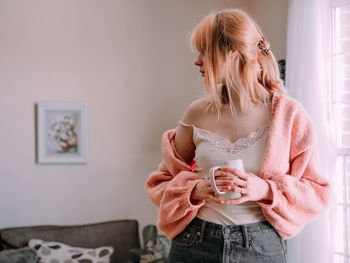 Portrait of young woman standing near a window at home