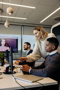 Businesswoman assisting male colleague over computer at desk in coworking office