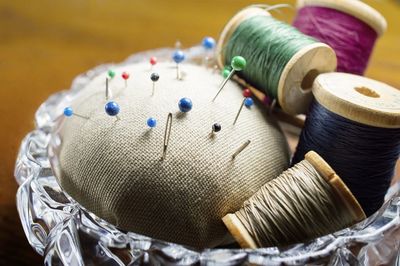 Close-up of pin cushions and spools in containers on table