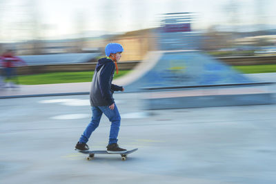 Side view of young skater wearing blue helmet in motion at skatepark