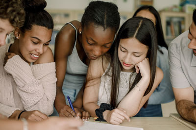 Female writing in book while friends and professor looking in classroom