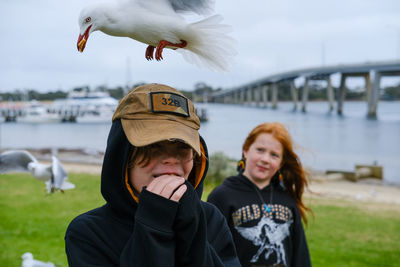 Portrait of young woman and young man standing against sea laughing at swooping seagulls