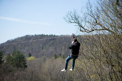 Man hanging on zip line by trees at forest