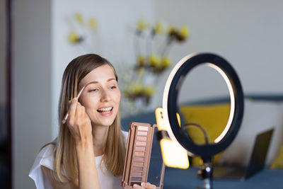 Portrait of a smiling young woman applying make-up at home