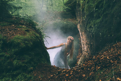 Young woman standing by rock at forest