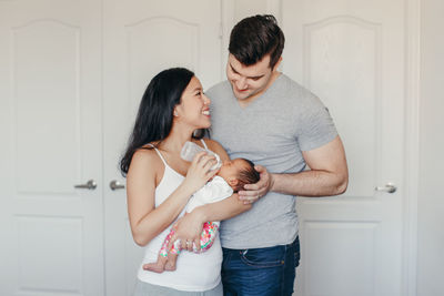 Man looking at wife feeding milk to daughter at home