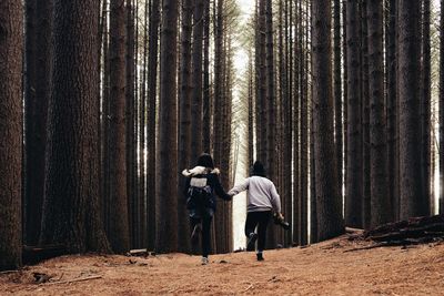 Rear view of friends running on dirt field in forest