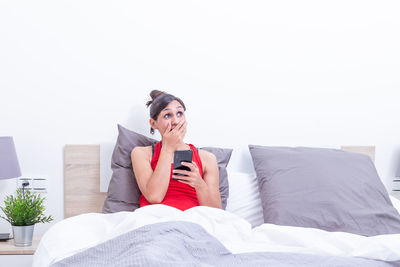 Young woman using mobile phone while lying on bed at home