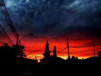 Low angle view of silhouette electricity pylon against dramatic sky