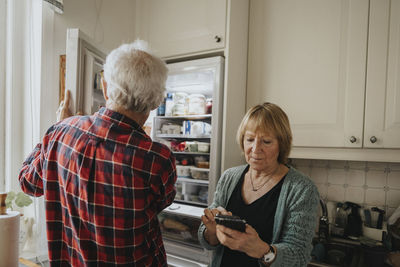 Senior couple opening fridge and using phone at home