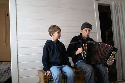 Grand father playing harmonica while sitting with grandson