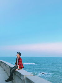 Man sitting on beach looking at sea against sky