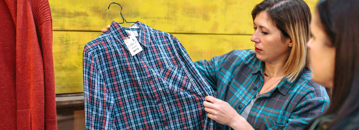 Banner of blonde woman employee showing plaid shirt to customer in vintage store