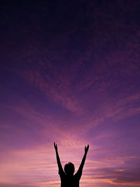 Silhouette man with arms raised against sky during sunset