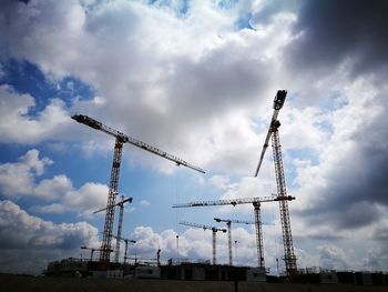 Low angle view of cranes at construction site against sky