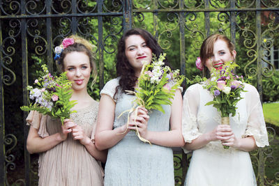 Portrait of friends with bouquet standing against gate